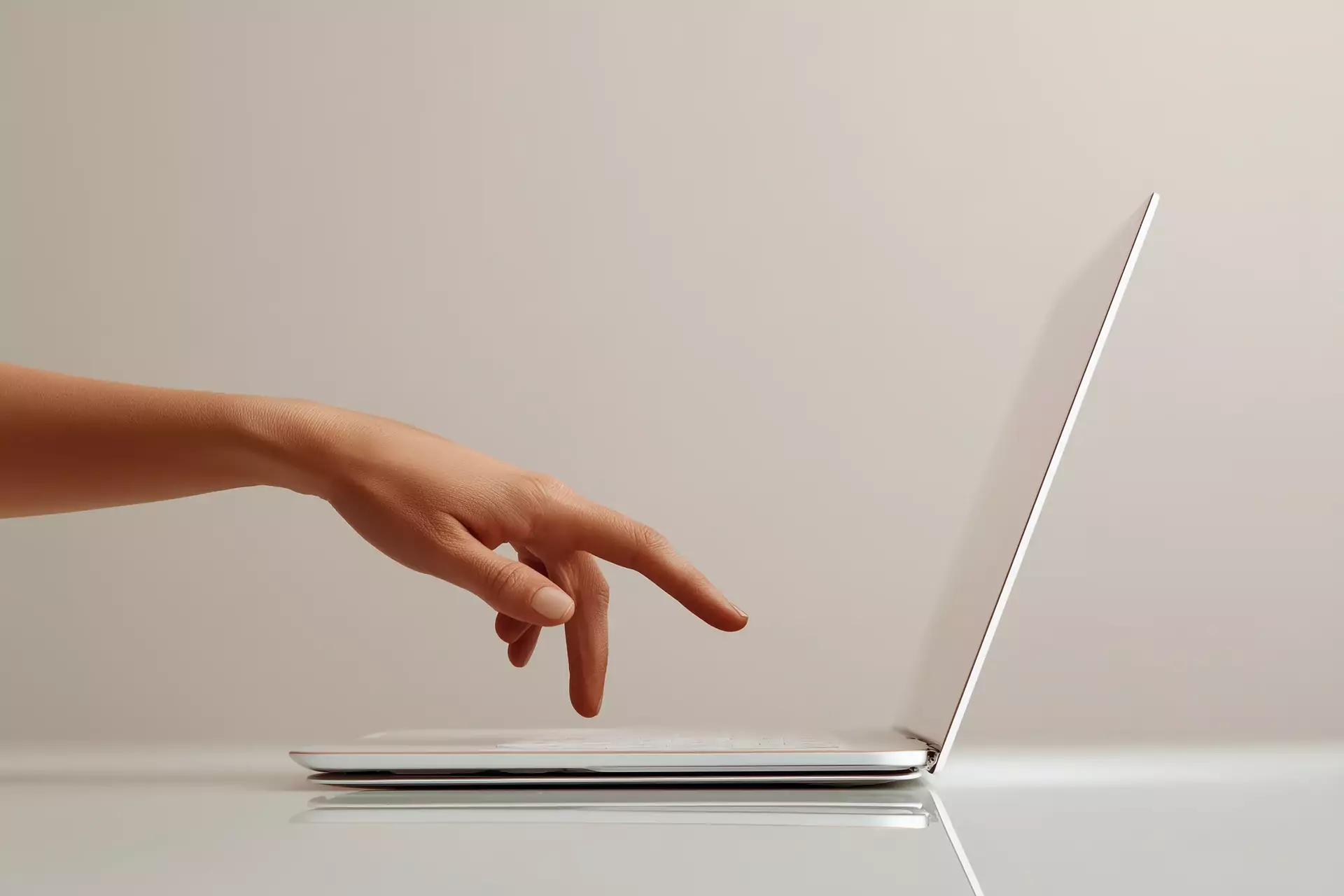 A hand reaching for a laptop on a desk