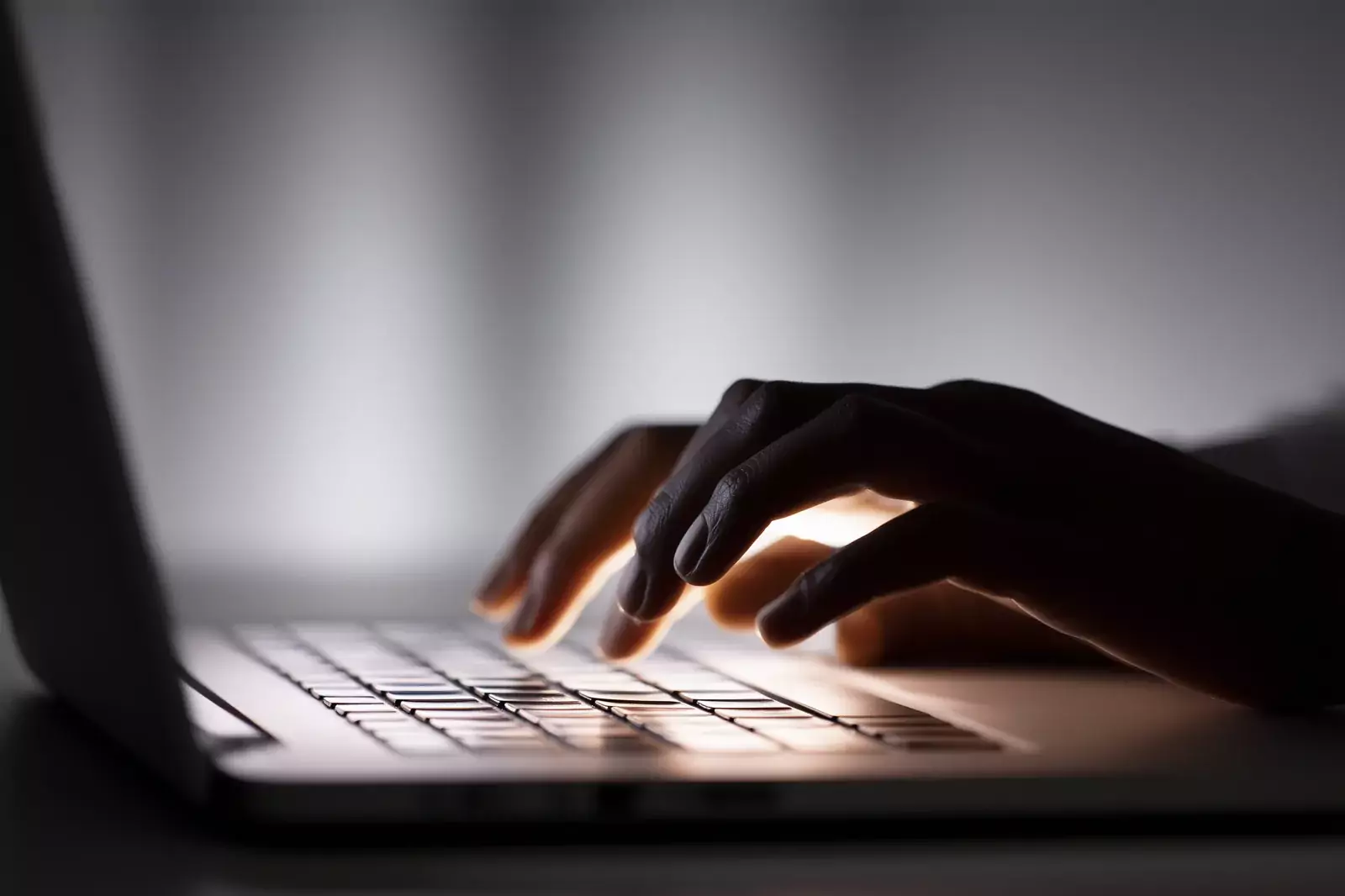 Hands typing on a laptop keyboard in low light