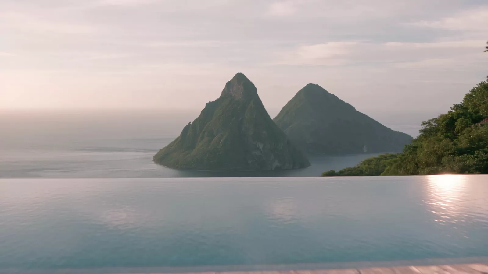 An infinity pool meeting the sea, with two steep green peaks across the bay