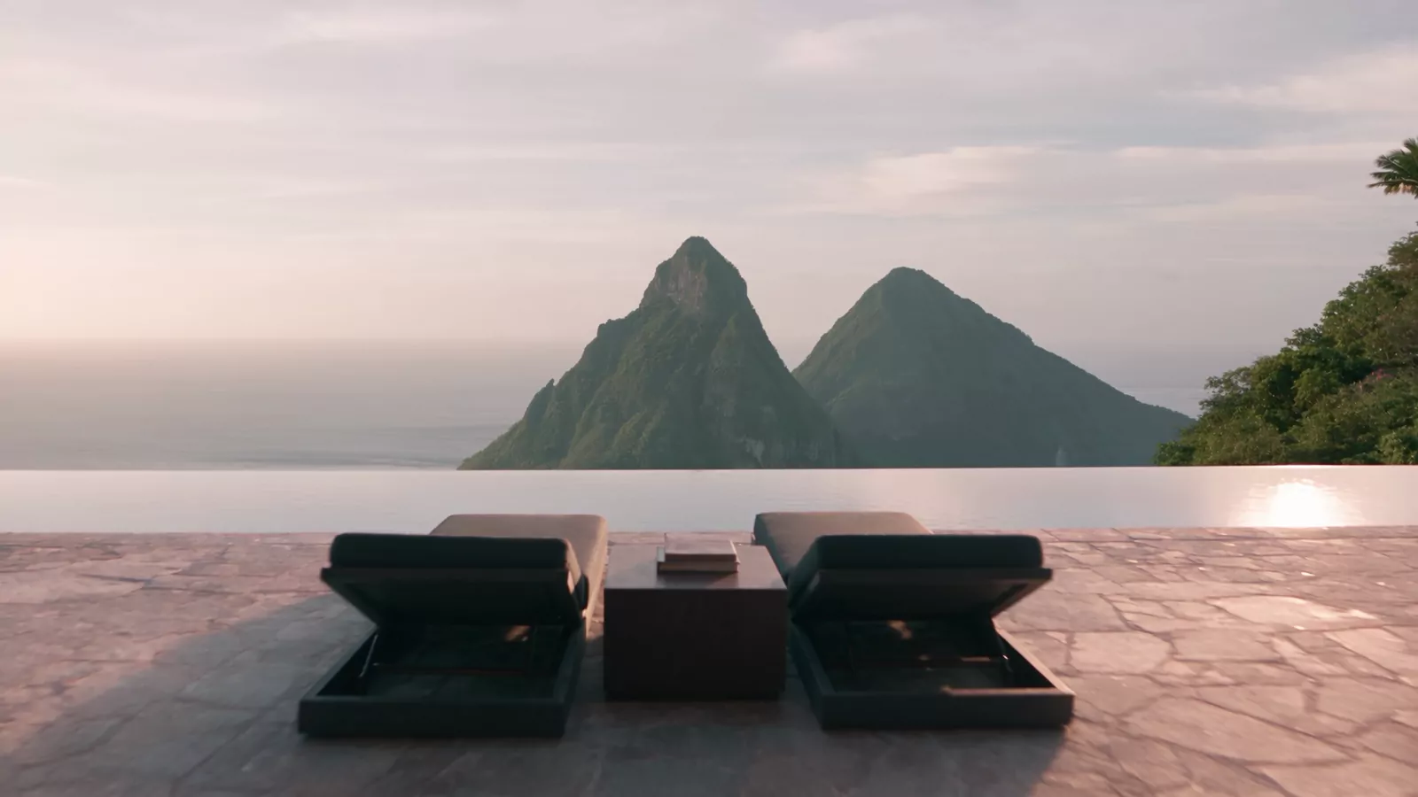 Two loungers on a stone terrace in front of an infinity edge and two green peaks